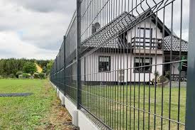 Nowoczesne, grafitowe ogrodzenie panelowe z podmurówką betonową, widok z boku na tle domu jednorodzinnego i zielonego trawnika.