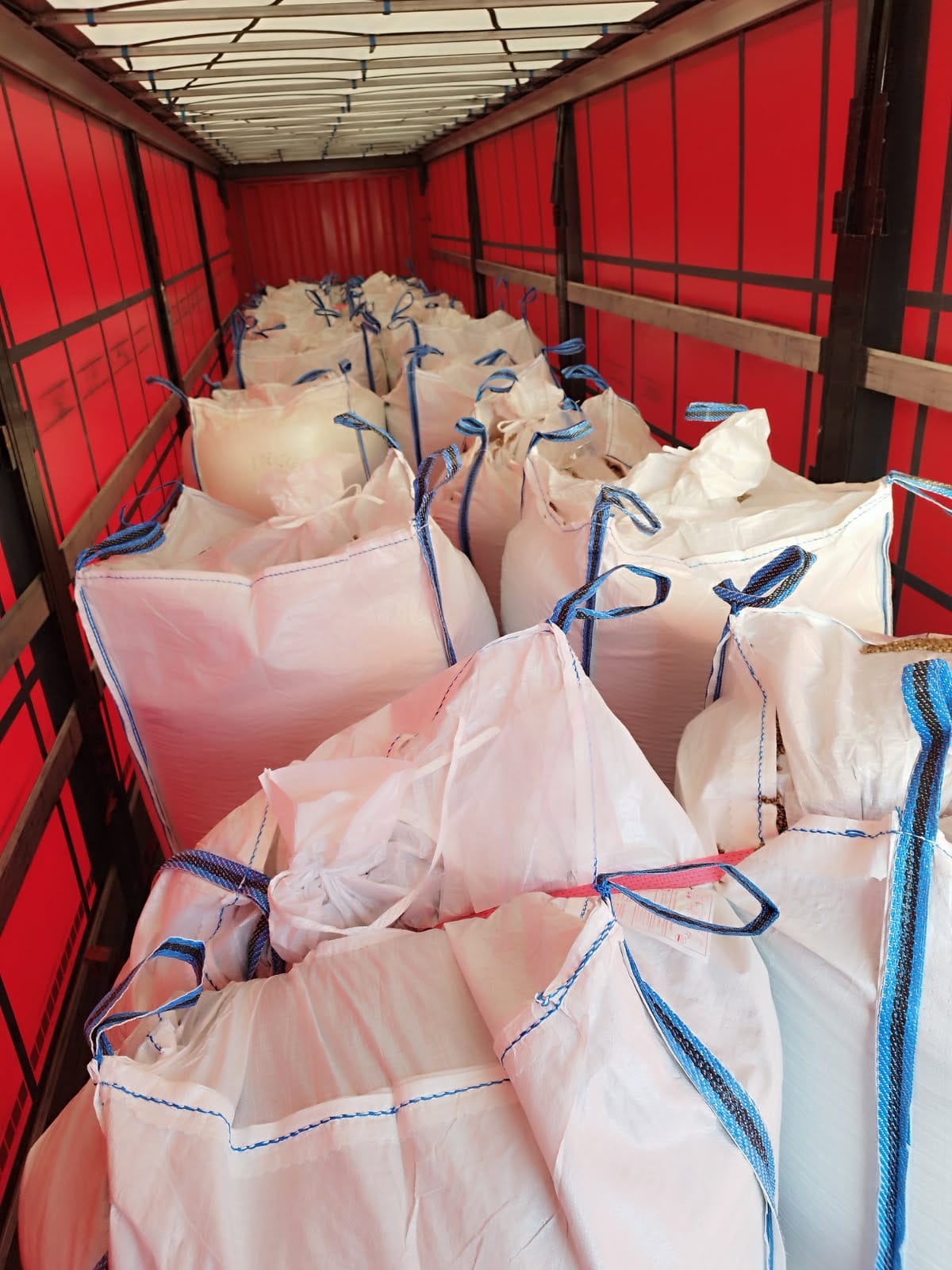 Wnętrze naczepy wypełnionej białymi workami typu big bag z niebieskimi uchwytami, widok z góry na załadunek, czerwone ściany naczepy.