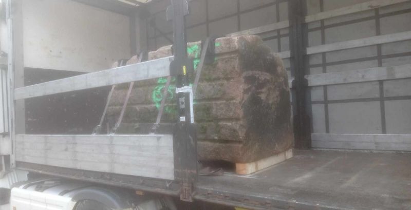 Ciężarówka z zabezpieczonym ładunkiem kamiennych bloków na paletach, widoczne pasy mocujące i elementy konstrukcji naczepy. Transport materiałów budowlanych.