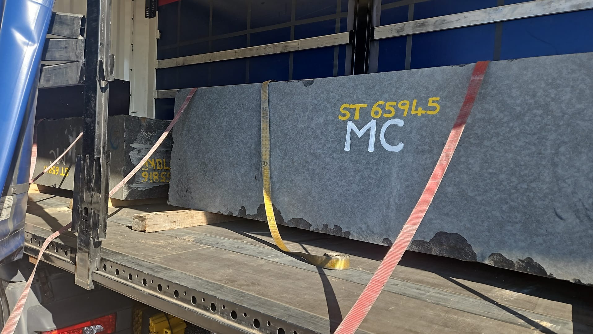 Transport ciężkich bloków kamiennych na paletach wewnątrz naczepy, zabezpieczonych pasami transportowymi. Widoczne oznaczenia 'ST 6594.5 MC'.
