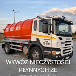 Pomarańczowo-biała cysterna asenizacyjna marki Scania z numerem telefonu firmy, zaparkowana na kostce brukowej, w tle widoczne zabudowania i błękitne niebo z chmurami.