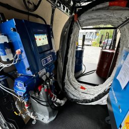 Ociepleniapoddaszy.pl - Wnętrze furgonetki z profesjonalnym agregatem natryskowym marki Graco, przeznaczonym do aplikacji pianki izolacyjnej, widoczne beczki z komponentami i zwinięte węże.