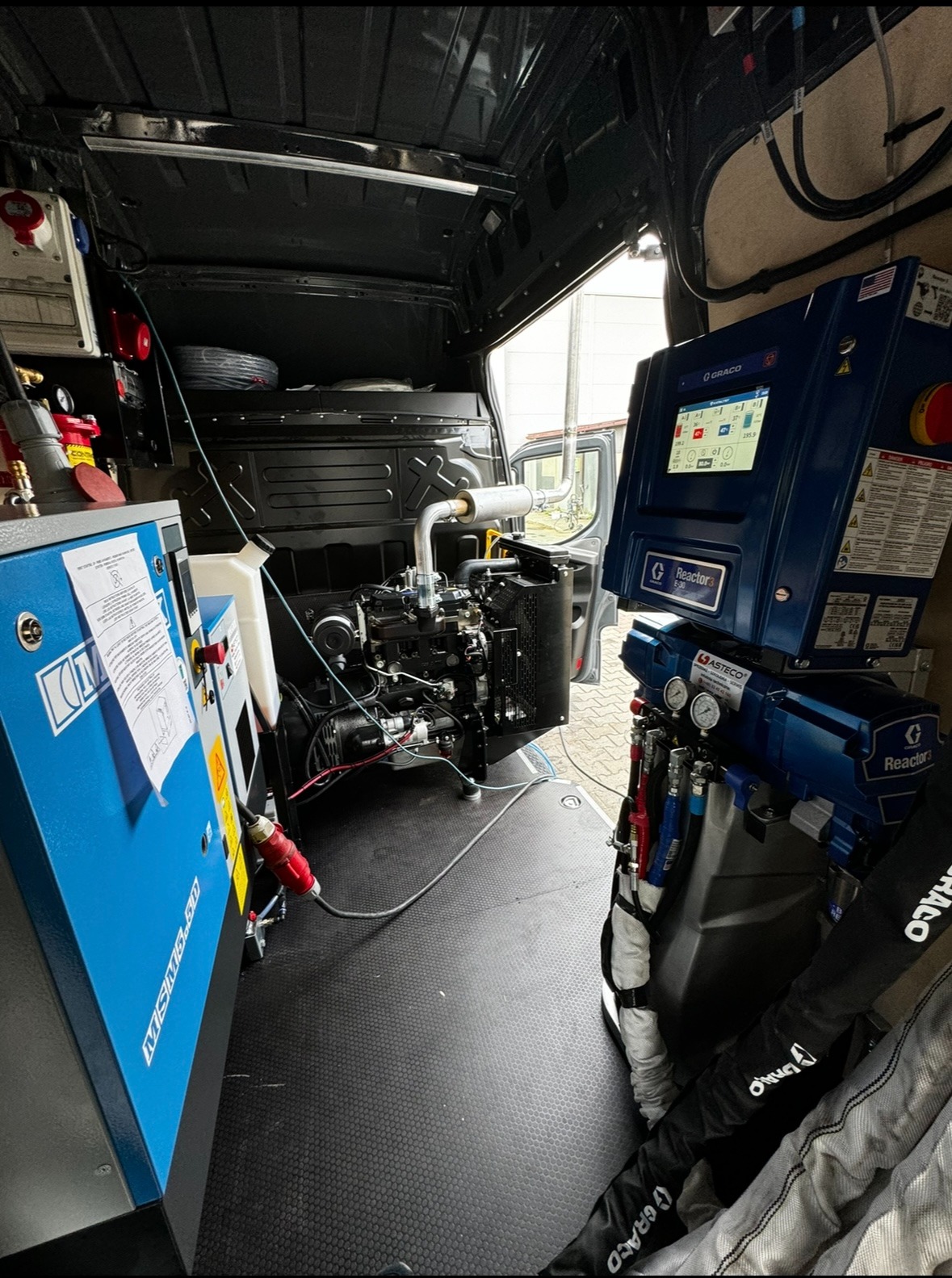 Wnętrze furgonetki z zamontowanym sprzętem do natrysku pianki PUR, widoczny agregat Graco Reactor 3 E-30, kompresor Asteco i silnik spalinowy, gotowe do mobilnego ocieplania.