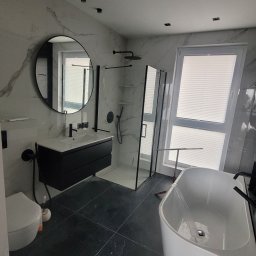 Top Bud Tomas Caputa - Nowoczesna łazienka z czarnymi akcentami: okrągłe lustro, szafka pod umywalką, kabina prysznicowa typu walk-in i wolnostojąca wanna, oświetlenie punktowe.