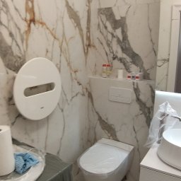 Top Bud Tomas Caputa - Nowoczesna łazienka z marmurowymi płytkami, wiszącą toaletą i umywalką na szafce, zabezpieczona folią ochronną przed zabrudzeniami podczas prac wykończeniowych.