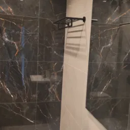 Ciemne płytki imitujące marmur z wyraźnym użyleniem w odcieniach bieli i brązu, zestawione z beżowymi płytkami oraz czarnym, metalowym wieszakiem na ręczniki.