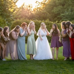 Mateusz Politański Herbaty z Nepalu - Panna młoda w białej sukni i druhny w kolorowych sukniach, stojące na trawie z zaskoczonymi minami na tle zieleni i zachodzącego słońca. Ujęcie z plenerowej sesji ślubnej.