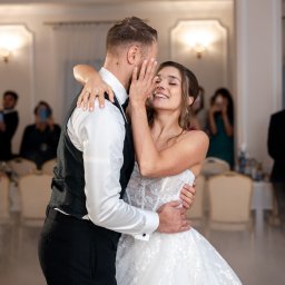 Mateusz Politański Herbaty z Nepalu - Uśmiechnięta panna młoda w objęciach pana młodego podczas pierwszego tańca, w tle goście weselni i dekoracje sali.