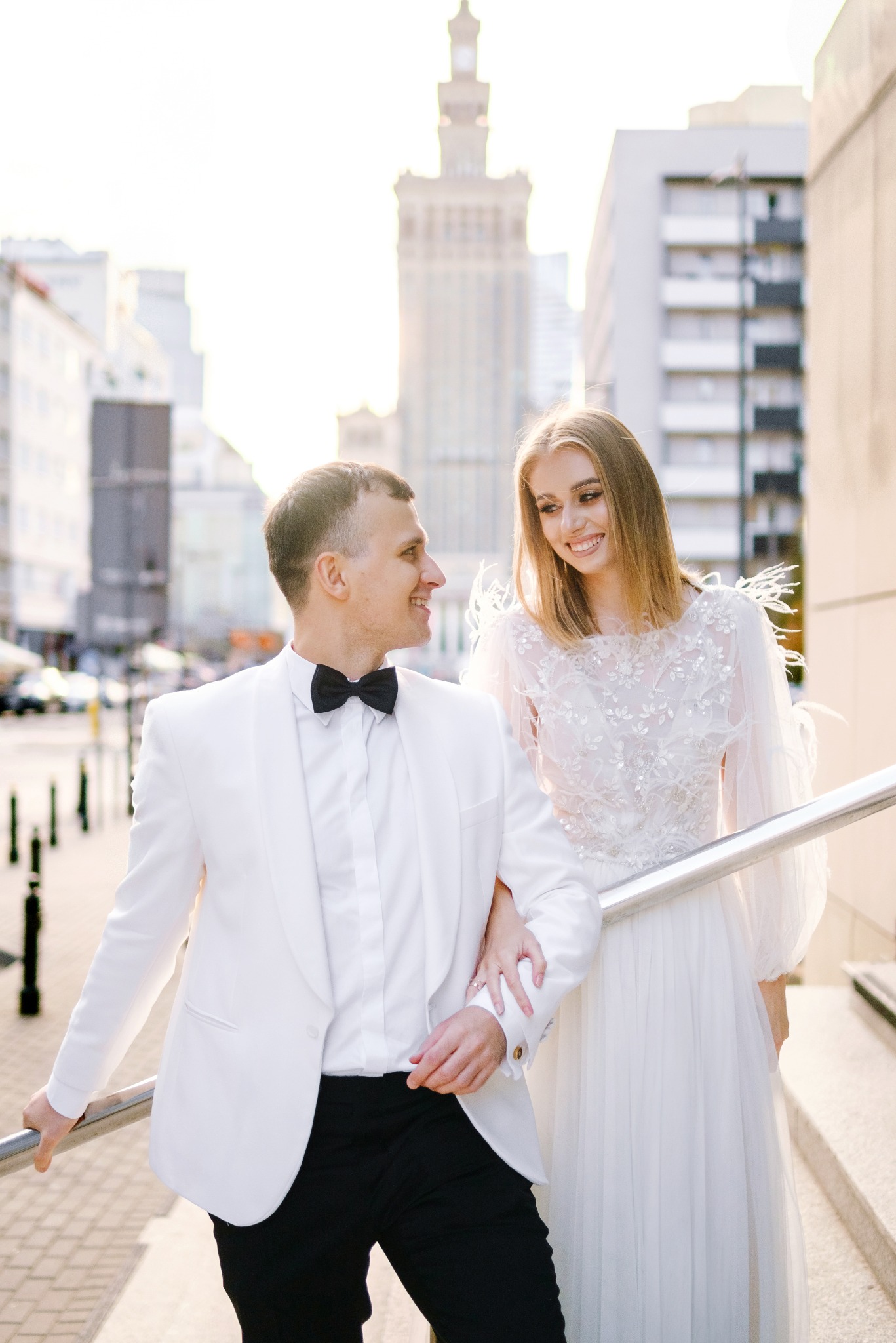 Uśmiechnięta para młoda w stylizowanych strojach spaceruje po mieście, w tle Pałac Kultury i Nauki w Warszawie.