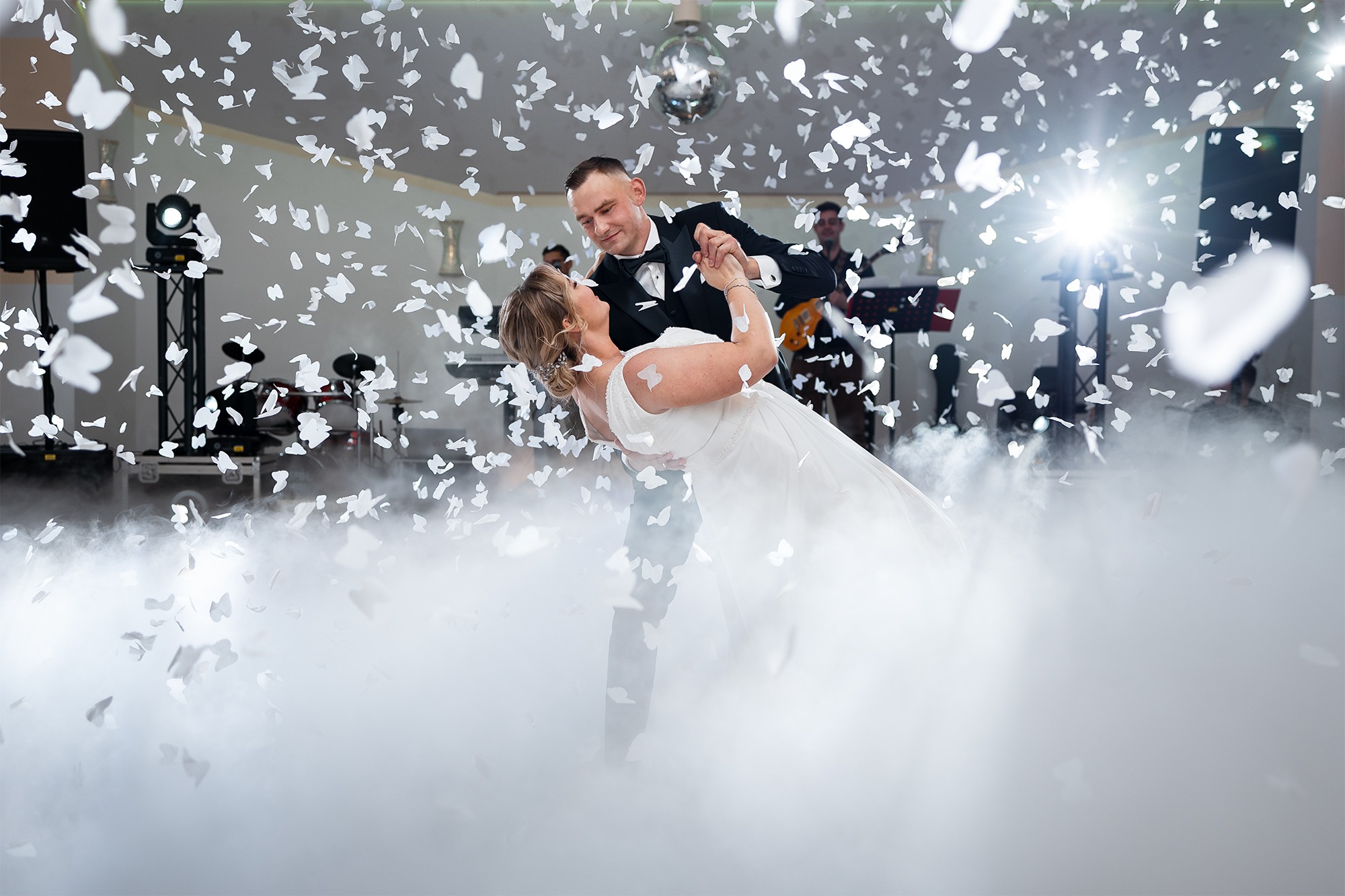 Para młoda w tańcu podczas wesela, otoczona konfetti i efektem mgły, w tle zespół muzyczny i oświetlenie eventowe.