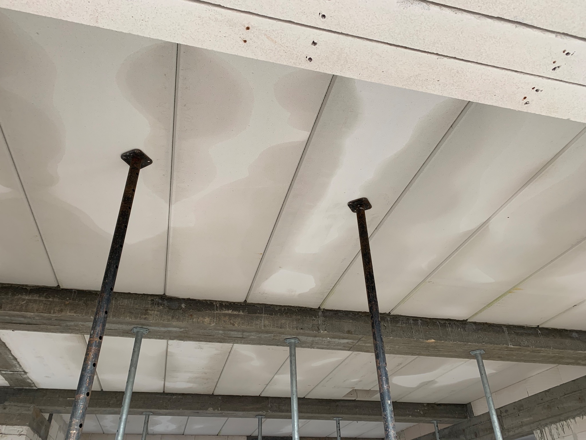 Szare podpory teleskopowe podtrzymujące biały strop z prefabrykatów podczas budowy domu.