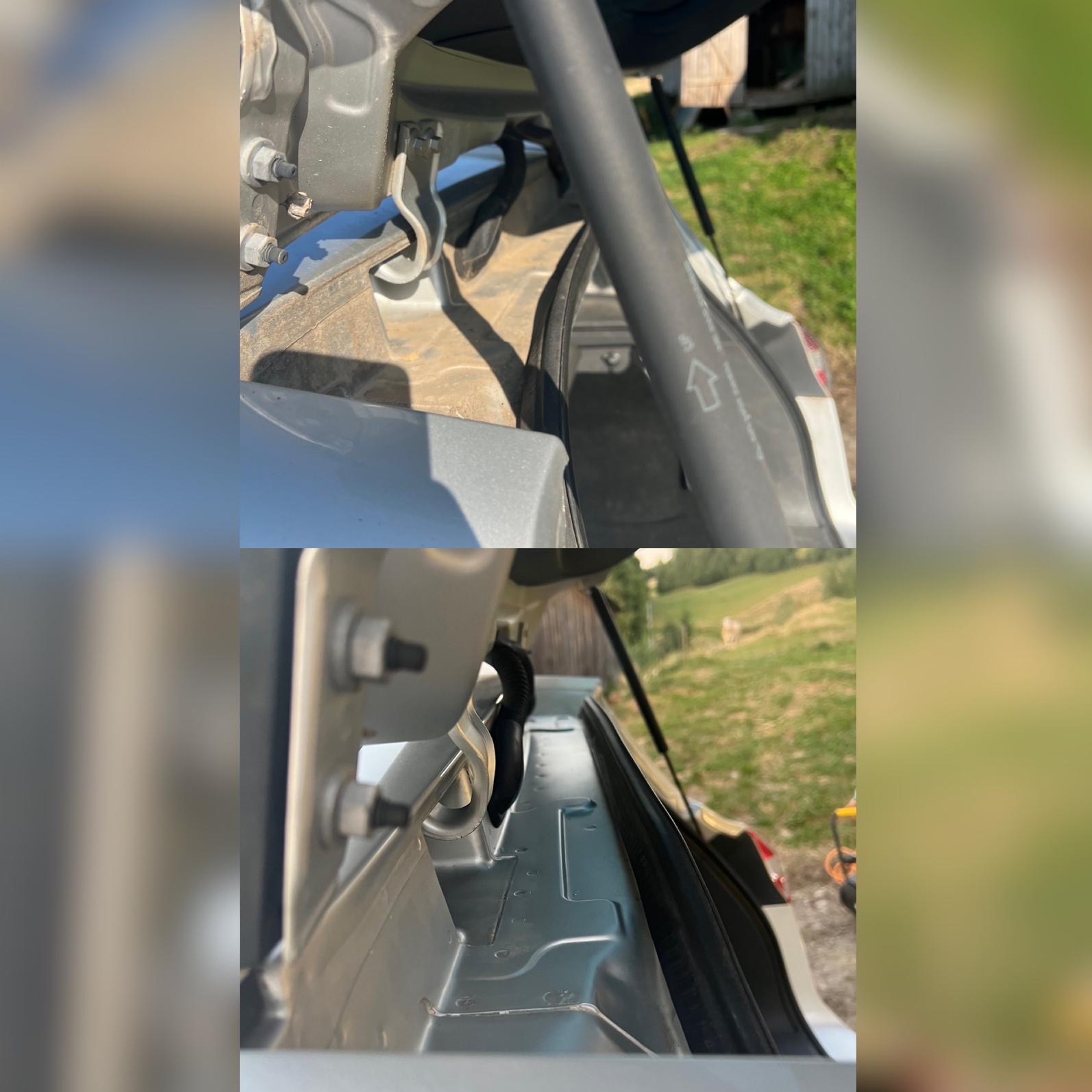 Wnętrze bagażnika srebrnego samochodu z widocznymi elementami mocującymi i siłownikiem, na zewnątrz trawa i budynek gospodarczy.