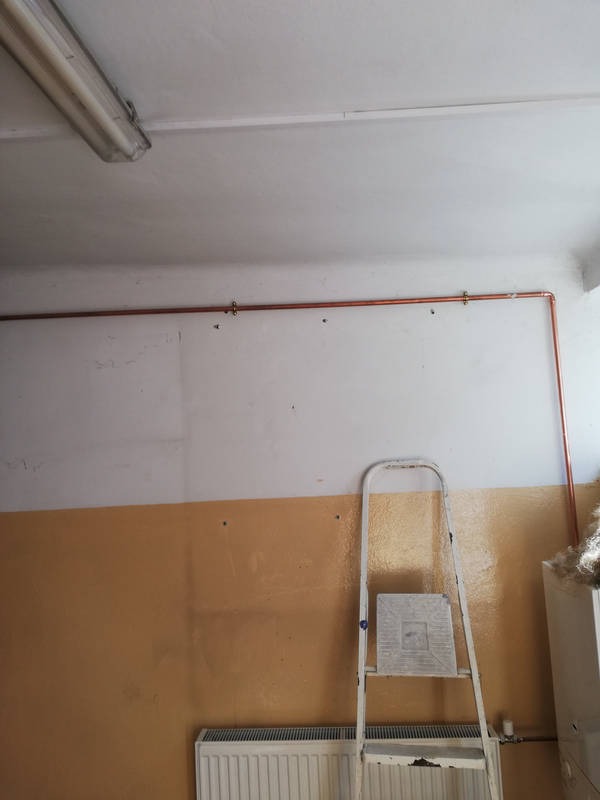 Miedziana rura centralnego ogrzewania zamontowana wzdłuż ściany nad grzejnikiem, widoczna drabina malarska.