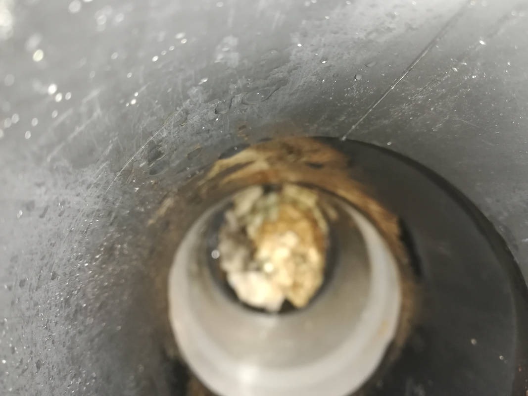 Wnętrze zatkanej, plastikowej rury odpływowej, widoczne z góry; nagromadzenie osadów i resztek organicznych blokuje przepływ.