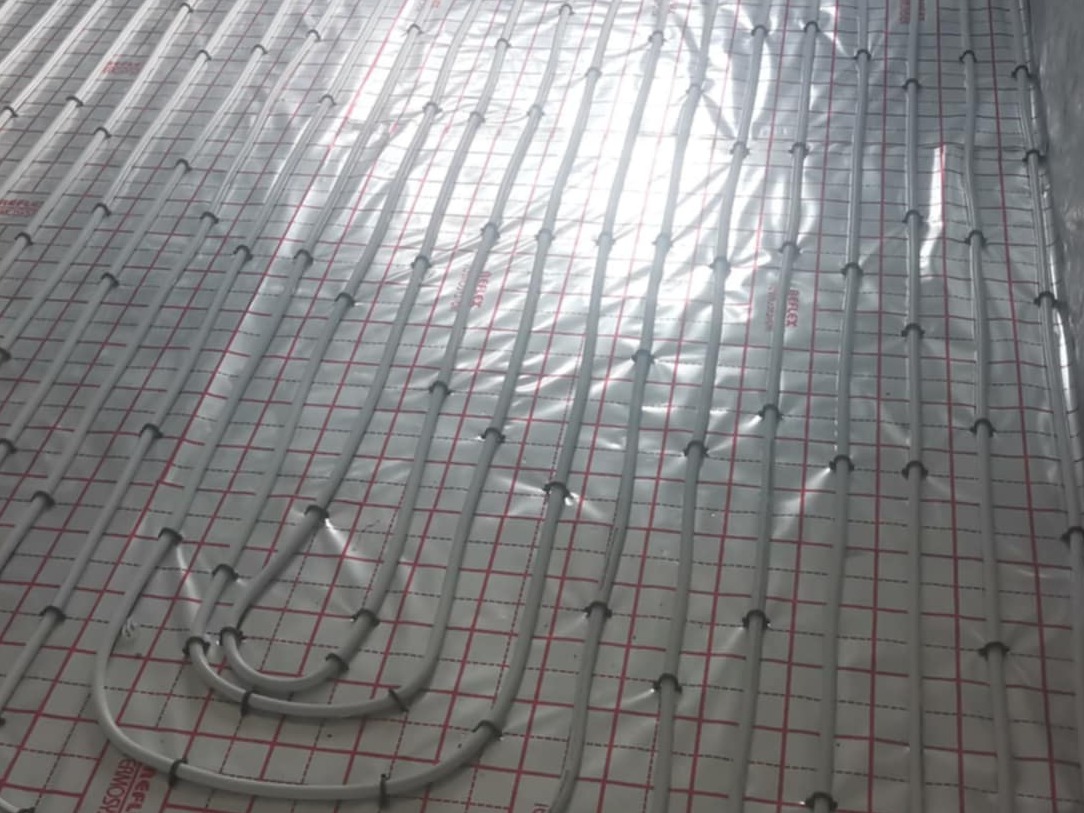 Ułożone rury ogrzewania podłogowego na folii z siatką, widoczne mocowania. Instalacja przed wylaniem posadzki, ułożona w pętle.