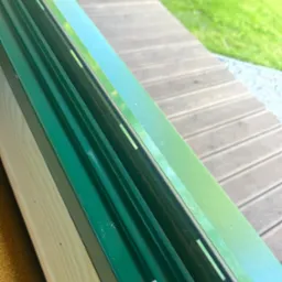 Zielony, czysty profil okienny po umyciu, widoczne drewniane elementy i fragment tarasu. Oświetlenie naturalne, słoneczny dzień.