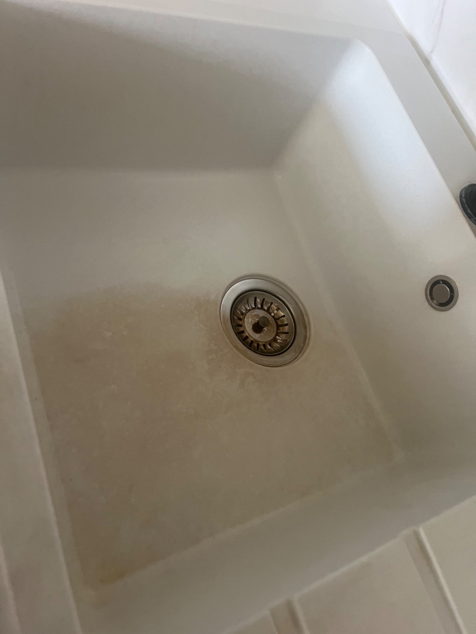 Zabrudzony, biały zlew kuchenny z widocznym odpływem i osadem. Zdjecie z bliska, z góry, ukazuje stan przed czyszczeniem.