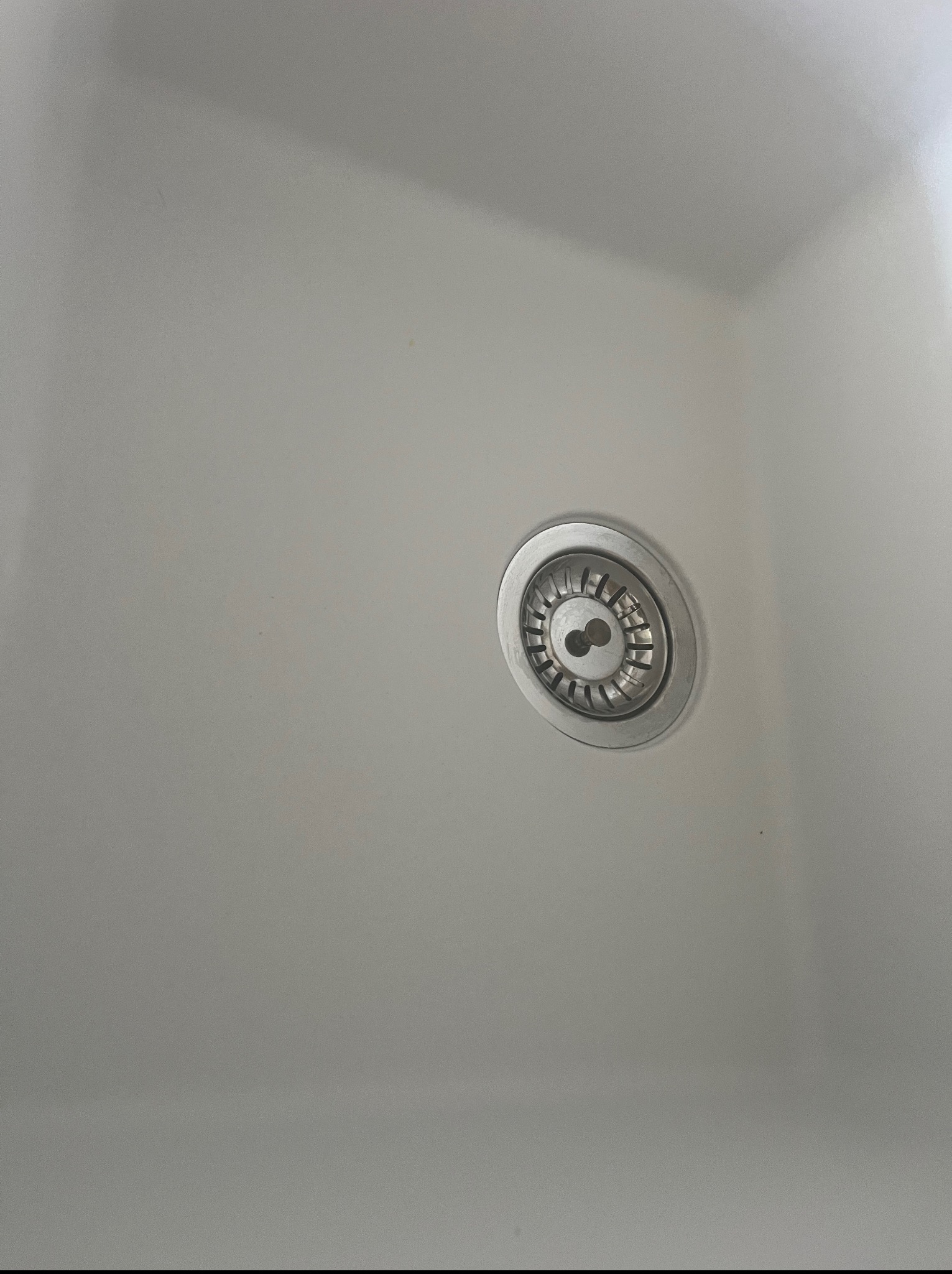 Biały zlew kuchenny z metalowym odpływem po czyszczeniu, widok z góry. Minimalistyczny design, czysta powierzchnia.