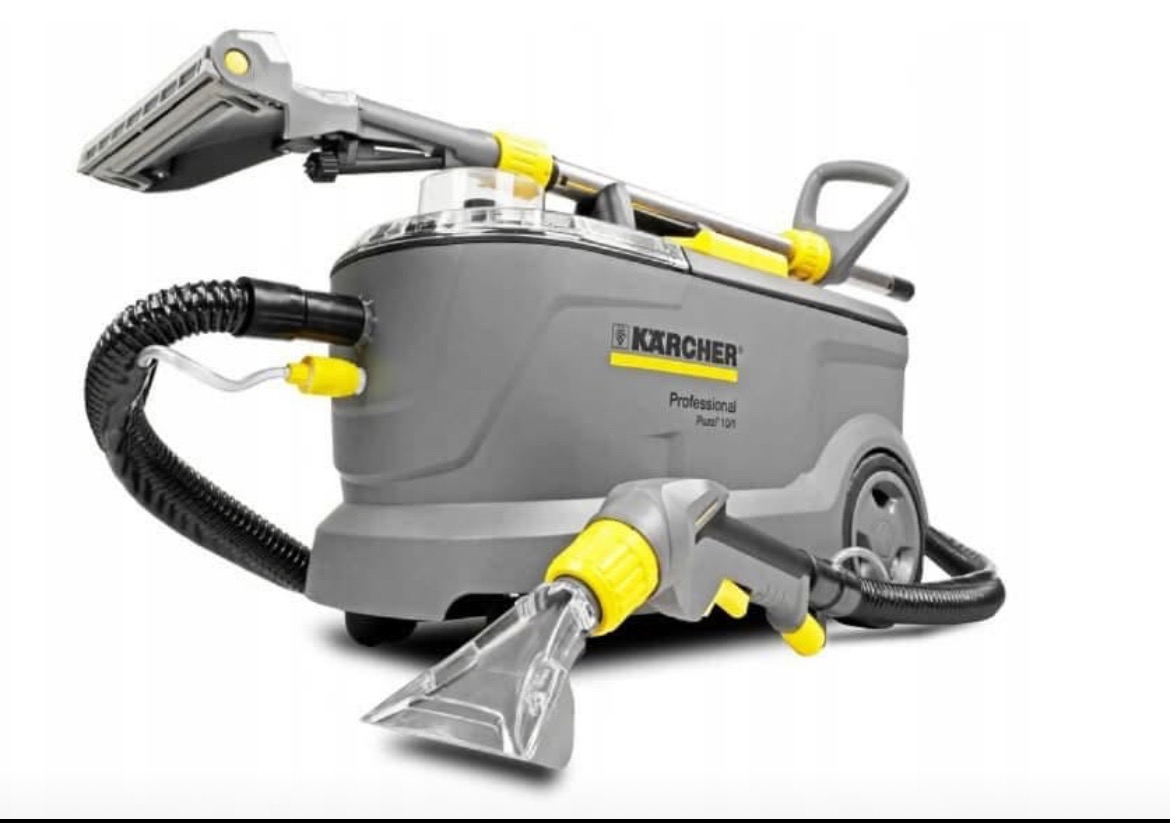 Profesjonalny odkurzacz piorący Kärcher Puzzi 10/1. Szaro-żółta obudowa, wąż ssący, dysza do tapicerki. Widoczne koła transportowe i uchwyt. Sprzęt do zadań specjalnych.
