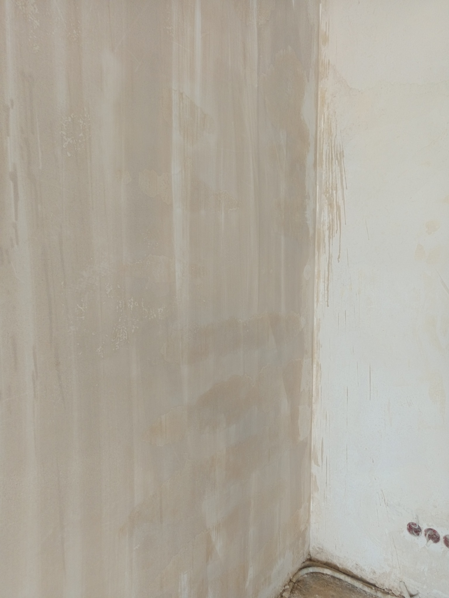 Ściana po nałożeniu gładzi, widoczne ślady szpachlowania, przygotowanie do malowania. Fragment rogu pokoju, instalacja elektryczna przy podłodze.