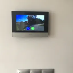 Zamontowany wideofon HiLook w Szczucinie, wyświetlający obraz z kamery zewnętrznej, poniżej widoczne trzy srebrne włączniki światła.