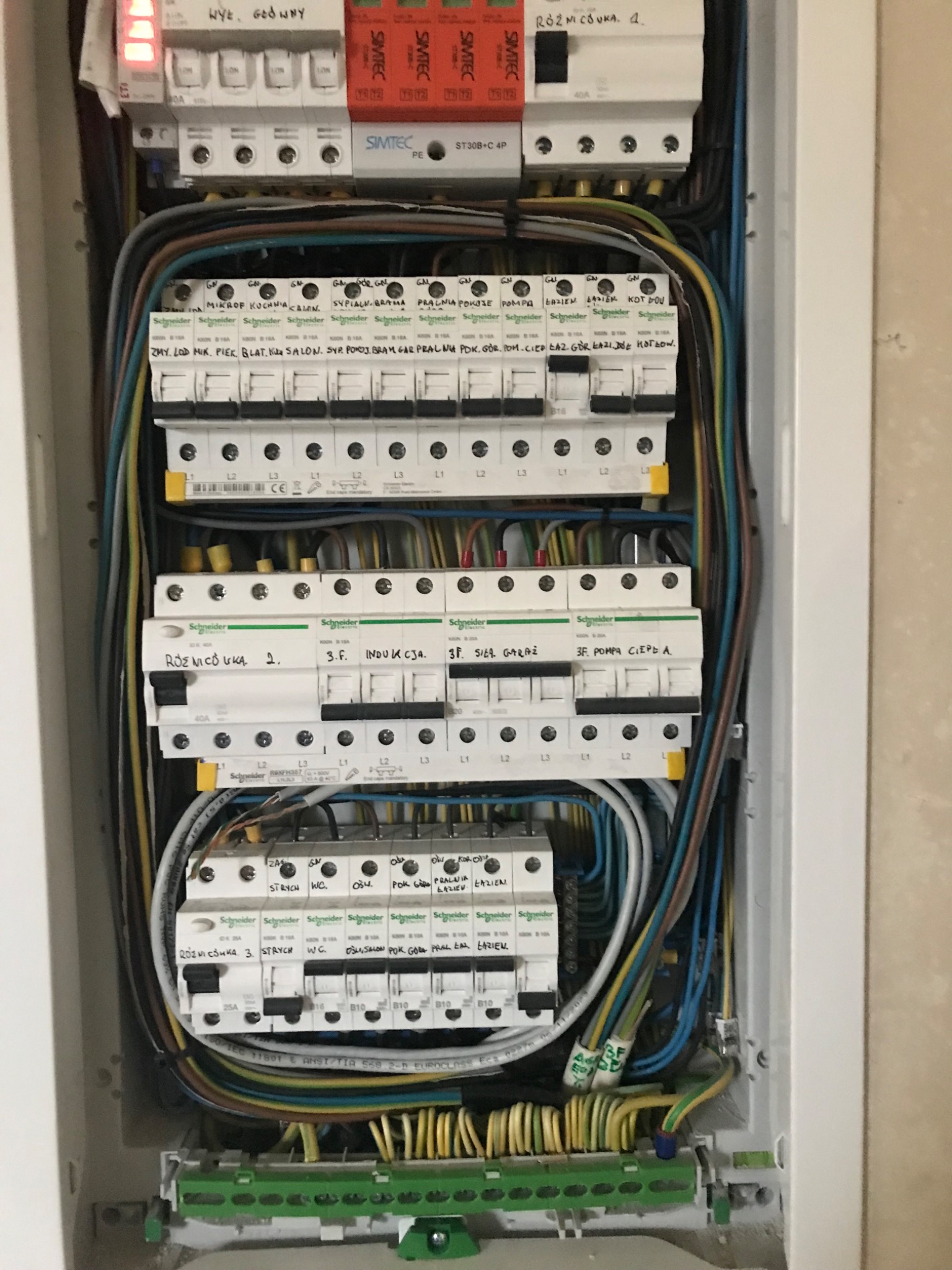 Rozdzielnia elektryczna z widocznymi bezpiecznikami, przewodami i oznaczeniami obwodów, z bliska, wewnątrz białej obudowy.