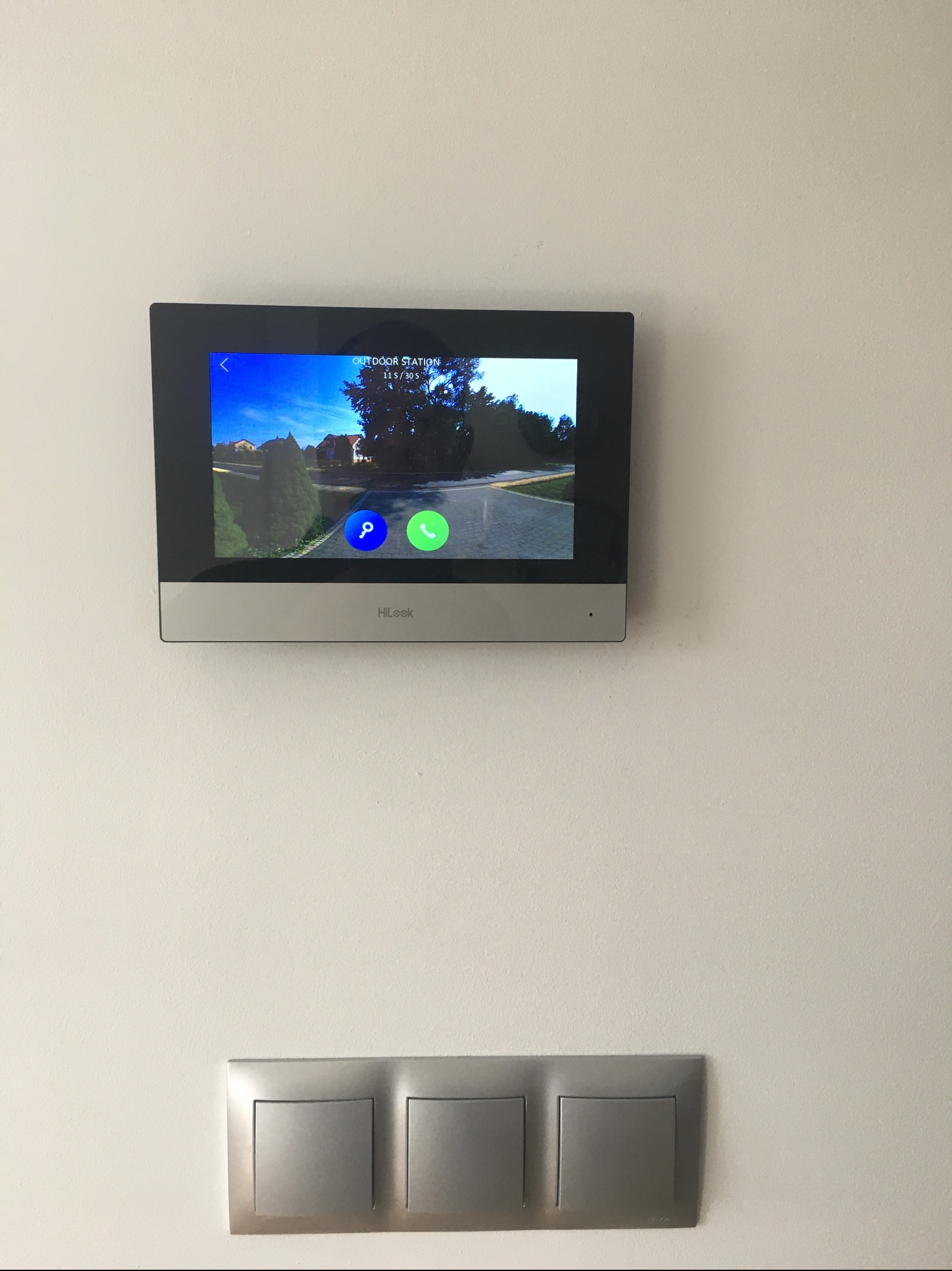 Zamontowany wideofon HiLook w Szczucinie, wyświetlający obraz z kamery zewnętrznej, poniżej widoczne trzy srebrne włączniki światła.