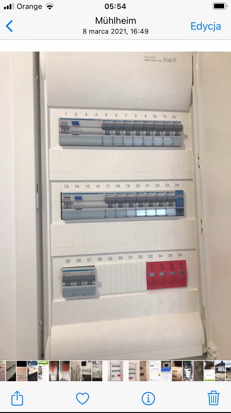 Otwarta skrzynka bezpiecznikowa Hager z numerowanymi wyłącznikami, widoczne trzy rzędy bezpieczników i czerwone zabezpieczenia przeciwprzepięciowe, ujęcie z bliska.