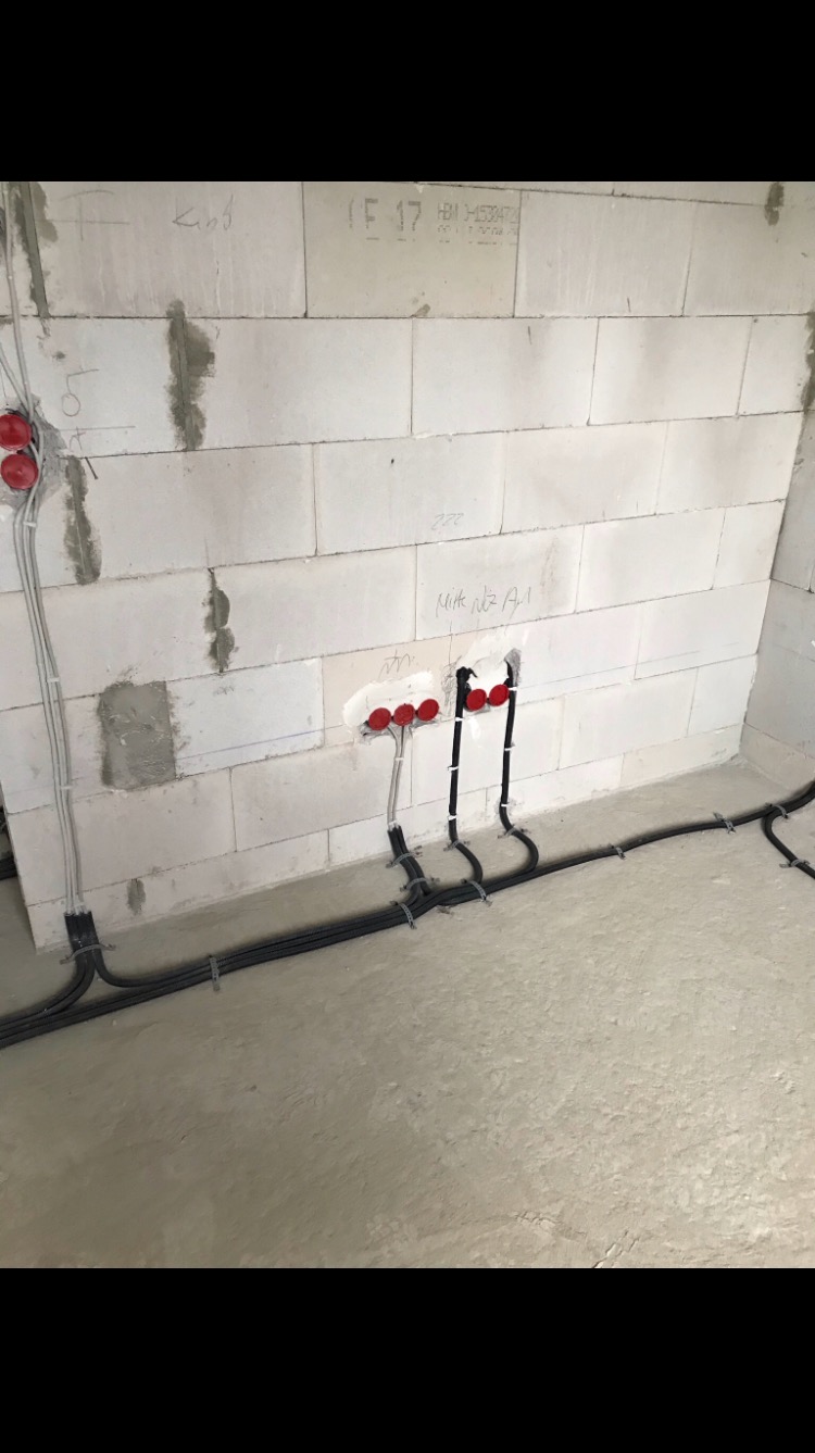 Wewnętrzne okablowanie elektryczne w surowym stanie, kable prowadzone po ścianie z betonu komórkowego, widoczne puszki instalacyjne z czerwonymi dekielkami.