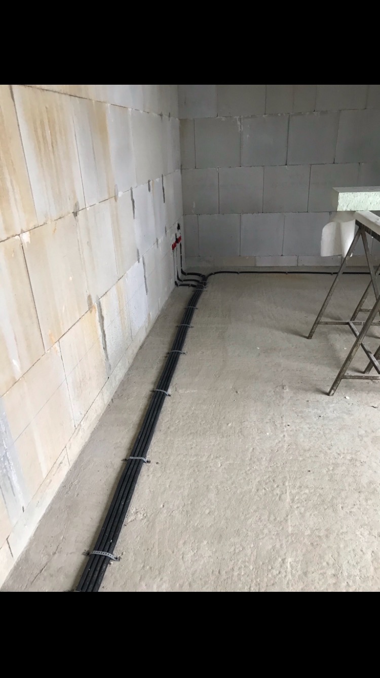 Wiązka czarnych kabli elektrycznych prowadzona wzdłuż ściany z białych bloczków w surowym wnętrzu, zabezpieczona opaskami zaciskowymi, z widocznym fragmentem drabiny malarskiej w tle.