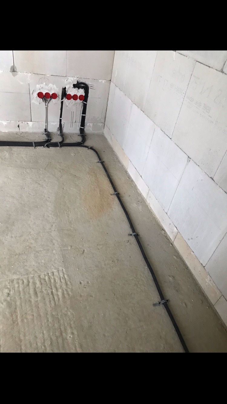 Surowe wnętrze w trakcie prac wykończeniowych; widoczne przygotowane wypusty instalacji wodno-kanalizacyjnej i czarne rury osłonowe kabli elektrycznych przy podłodze, przymocowane uchwytami...