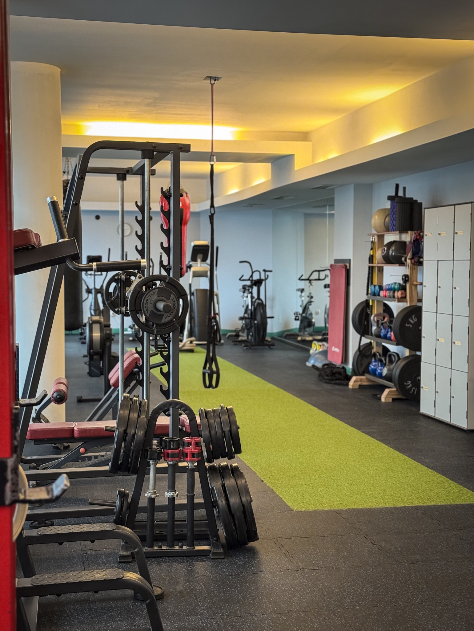 Wnętrze siłowni z różnorodnym sprzętem do ćwiczeń, w tym stojaki na obciążenia, maszyny do ćwiczeń cardio i worki treningowe, oświetlone ciepłym światłem.