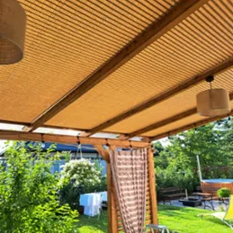 Zadaszenie tarasu z beżową tkaniną w paski, drewniana konstrukcja, widok na ogród z jacuzzi i suszącym się praniem.