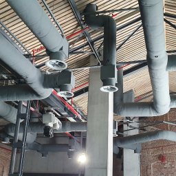 GRUPA DB - Malowanie rur wentylacyjnych na szaro w biurze z odsłoniętą cegłą, widoczny podnośnik koszowy.