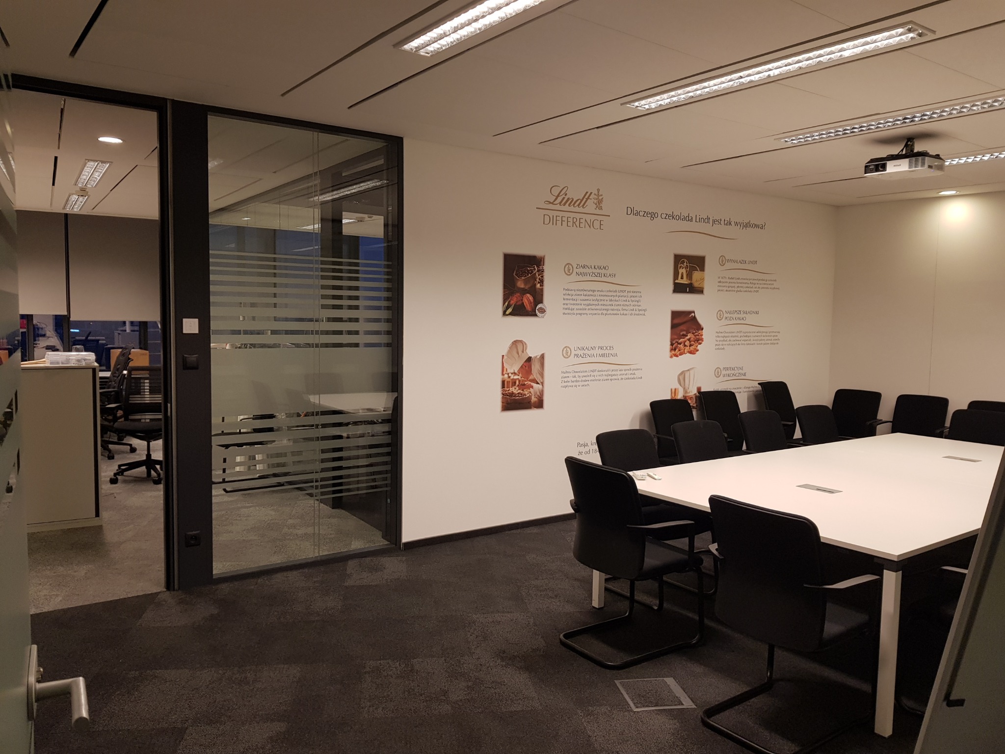 Nowoczesna sala konferencyjna z białym stołem, czarnymi krzesłami i przeszkloną ścianą, na której widnieje grafika Lindt Difference.