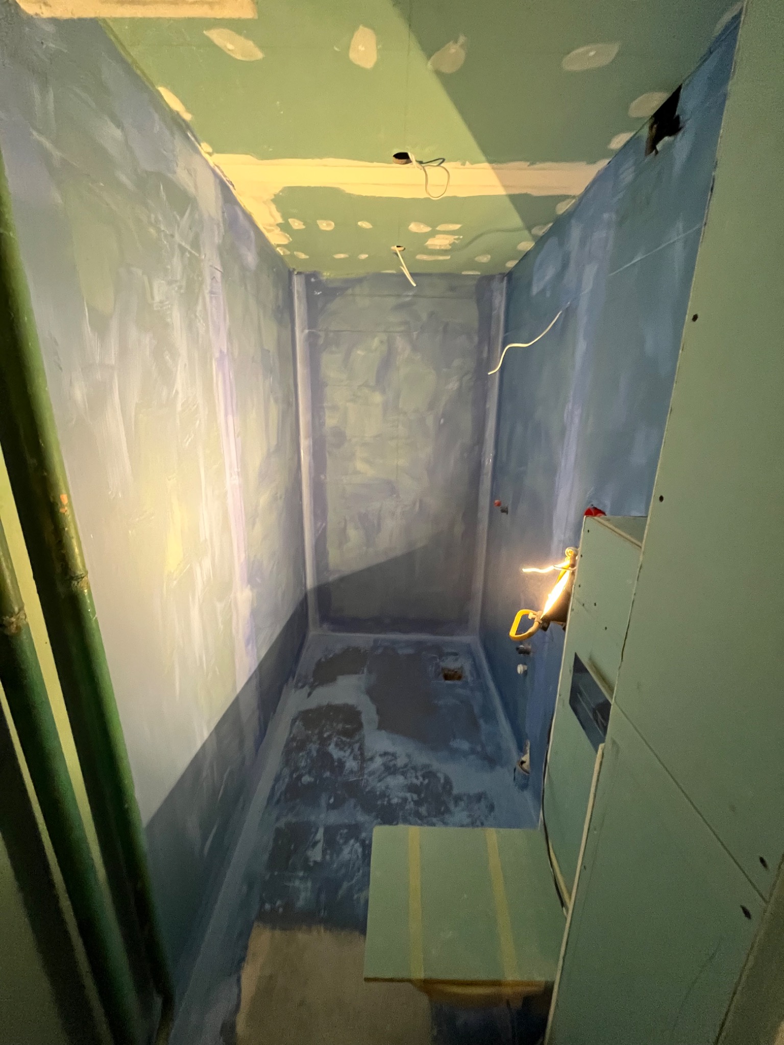 Wnętrze łazienki w trakcie remontu: surowe ściany przygotowane pod malowanie, widoczne ślady szpachlowania i gruntowania, fragment konstrukcji z płyty karton-gipsu oraz wystające kable elektryczne.