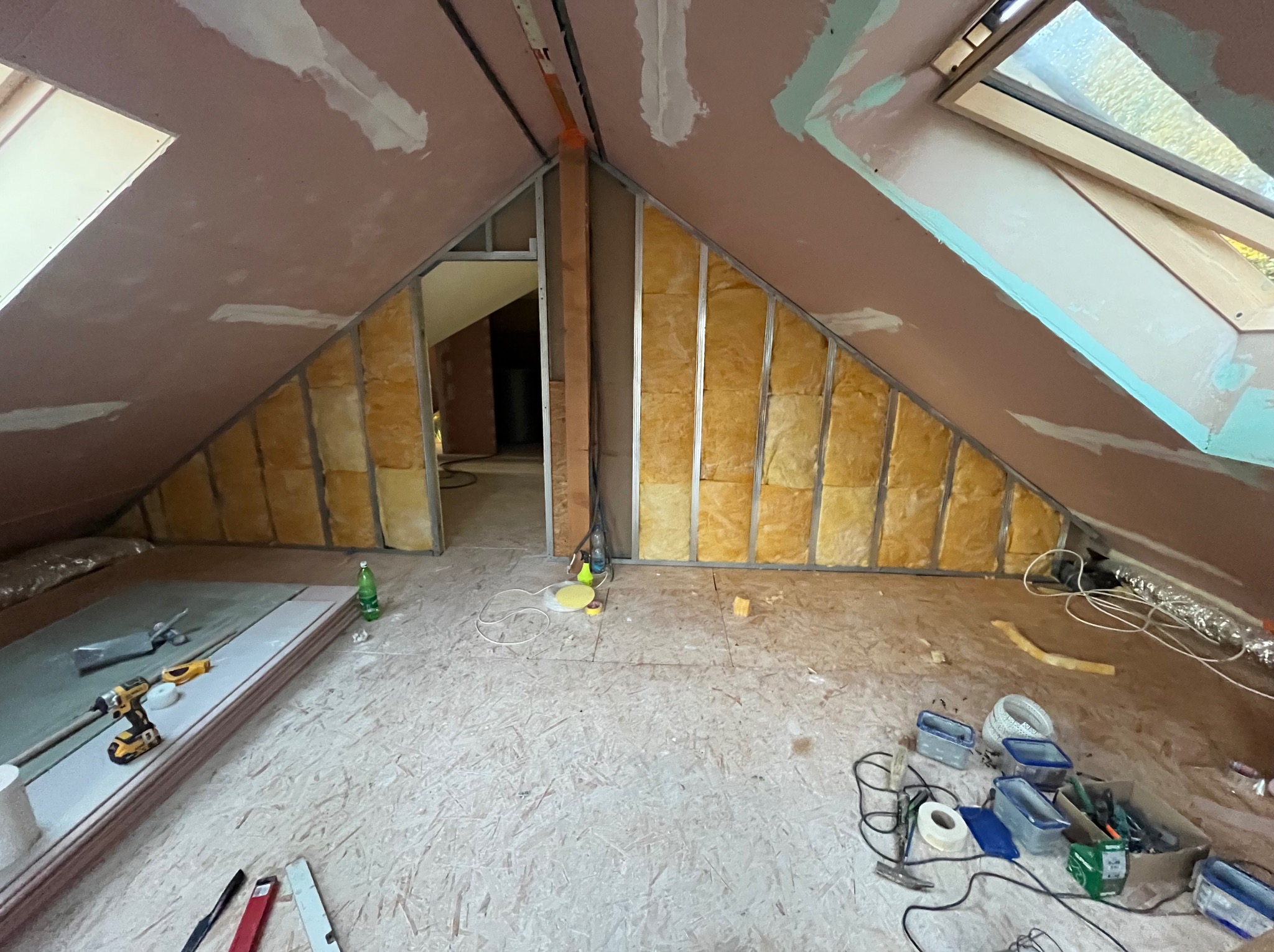 Poddasze w trakcie adaptacji: widoczne ocieplenie wełną mineralną w metalowym stelażu, płyty gipsowo-kartonowe częściowo zamontowane, szpachlowane łączenia, okna dachowe, narzędzia pracy...