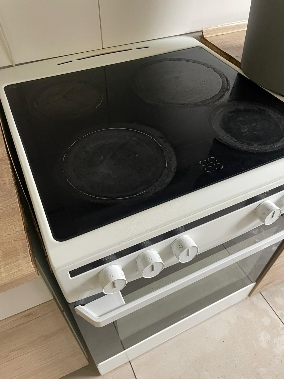 Biała kuchenka elektryczna z czarną płytą grzewczą, widoczne zabrudzenia na polach grzewczych, co sugeruje potrzebę sprzątania. Ujęcie z góry pod kątem.
