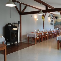 Restauracja Wola Verde - Sala bankietowa z długimi stołami nakrytymi białymi obrusami, krzesła z drewnianymi oparciami, dekoracje kwiatowe w wazonach, świece w szklanych świecznikach, balony, bufet ze słodkościami i tło...