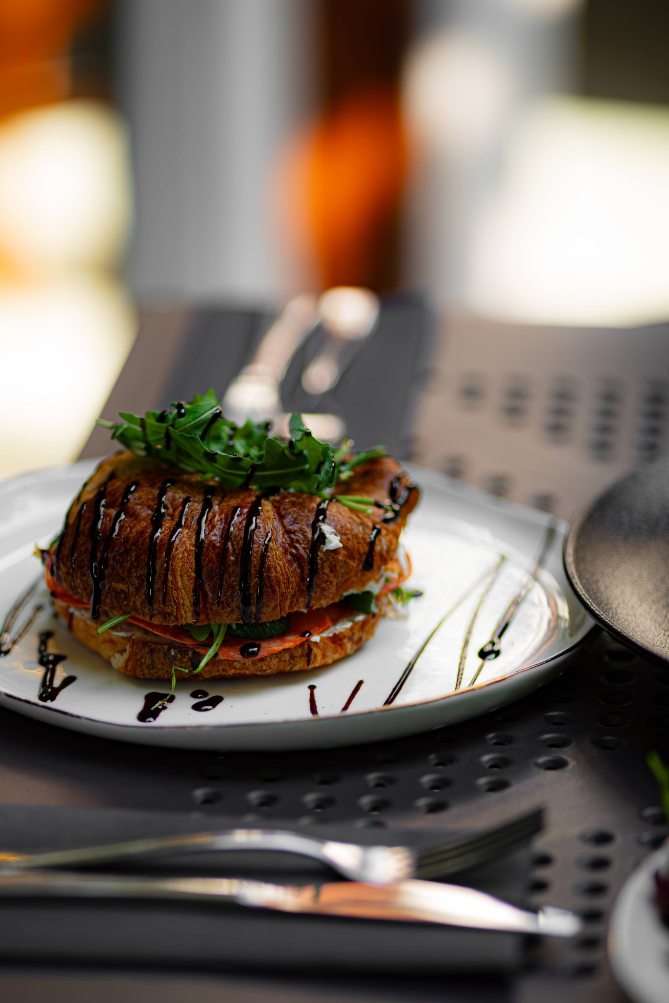 Kreatywnie podany croissant z szynką, serem, warzywami i sosem balsamicznym na białym talerzu z dekoracyjnymi smugami sosu.