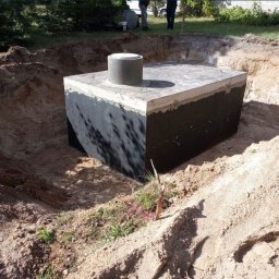 SGE GRZEGORZ GIL - Betonowy zbiornik z pokrywą, częściowo zagłębiony w ziemi w Strzelcach Krajeńskich, otoczony wykopem z piasku i ziemi, widoczne ślady świeżych prac ziemnych.