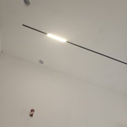 VT_PRO_MASTER - Biała ściana i sufit z zamontowaną czarną, podłużną lampą LED, widoczne otwory na oświetlenie punktowe i wystające kable ze ściany.