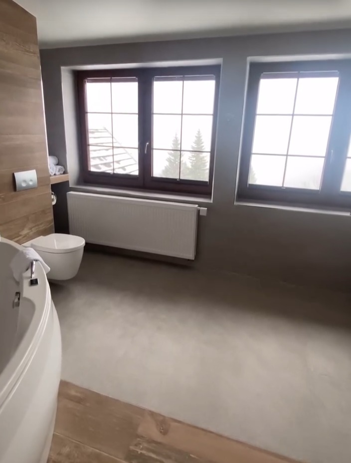 Nowoczesna łazienka w szarościach z drewnianymi akcentami, widok na zaśnieżone drzewa przez okna