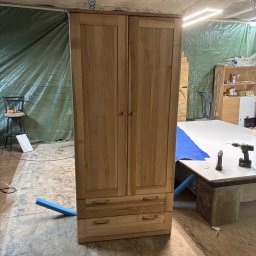 stolart - Dwudrzwiowa, drewniana szafa z dwiema szufladami na tle warsztatu z narzędziami i folią ochronną.