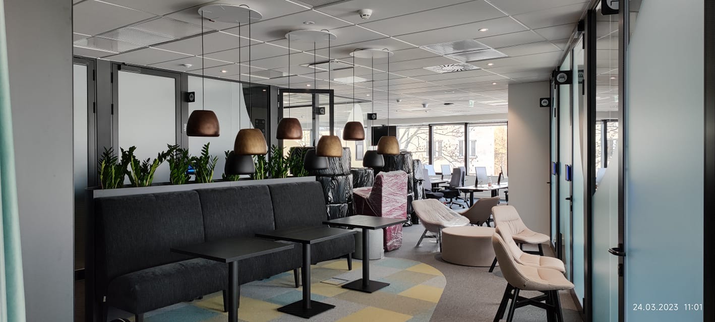 Nowoczesne biuro z sofą, stolikami, krzesłami i lampami wiszącymi o różnych odcieniach brązu, widoczne także rośliny i meble zabezpieczone folią.