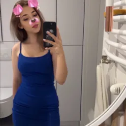 Młoda kobieta robi selfie w łazience z filtrem z uszami i nosem pieska, widoczna umywalka, grzejnik drabinkowy i białe szafki.