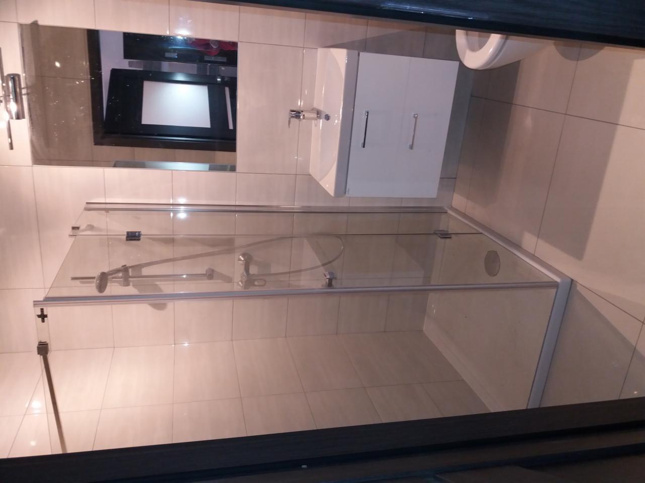 Nowoczesna kabina prysznicowa z transparentnego szkła, biała umywalka z szafką, lustro i jasne płytki w wykończonej łazience.