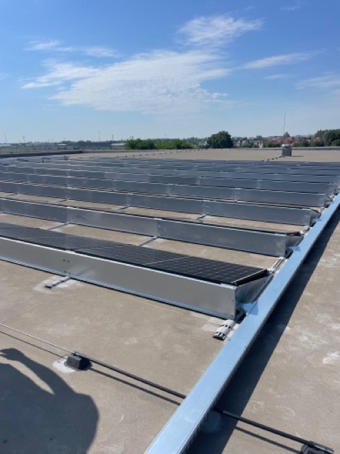 Rzędy aluminiowych konstrukcji wsporczych na płaskim dachu, przygotowanych pod montaż paneli słonecznych, widok z góry w słoneczny dzień.