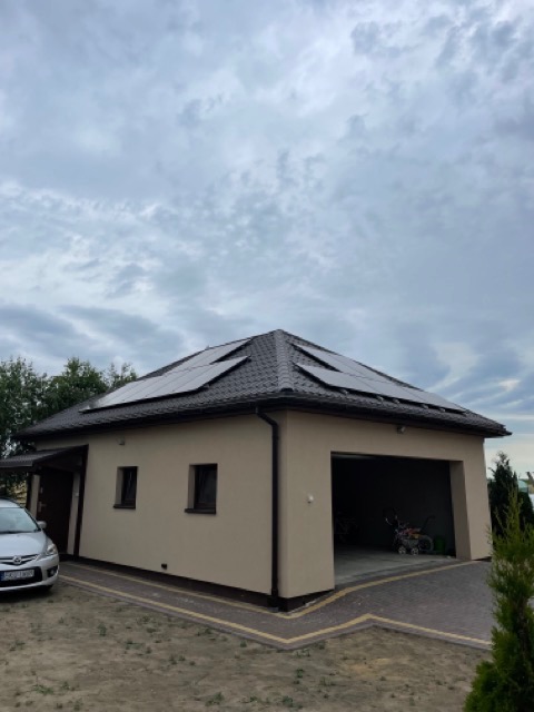 Dom z garażem i panelami słonecznymi na dachu, widok z zewnątrz w pochmurny dzień.