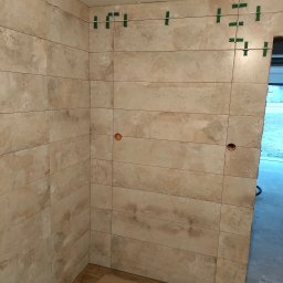 Usługi Ogólnobudowlane Rafał Bartyzel - Ściana wyłożona beżowymi, prostokątnymi płytkami ceramicznymi w trakcie montażu, z widocznymi krzyżykami dystansowymi i otworami na gniazdka elektryczne.